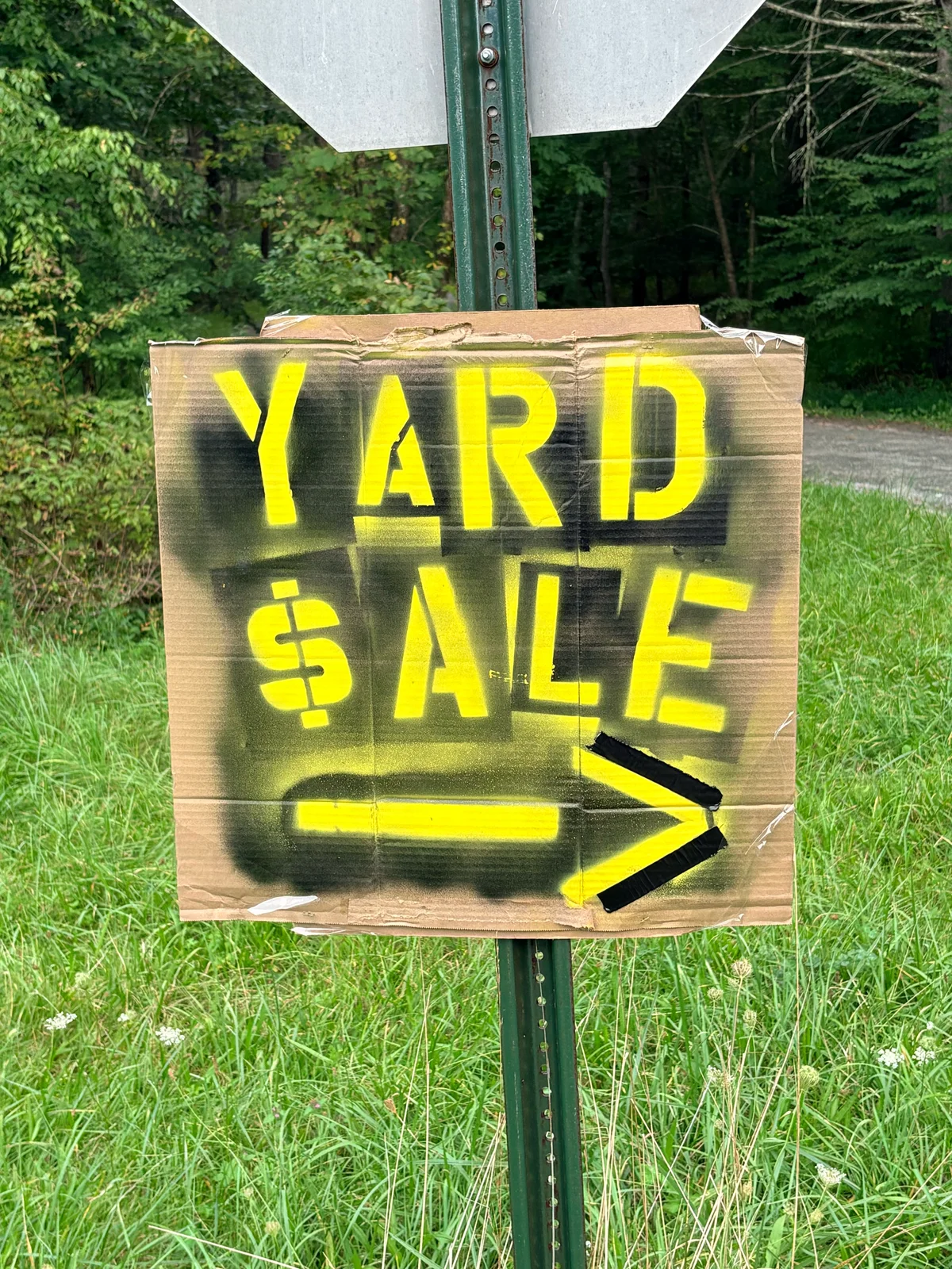 A handmade cardboard yard sale sign with bright yellow lettering and an arrow pointing right